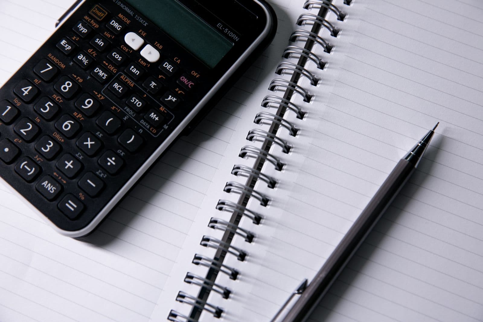 Calculator and pen on an open lined notebook.
