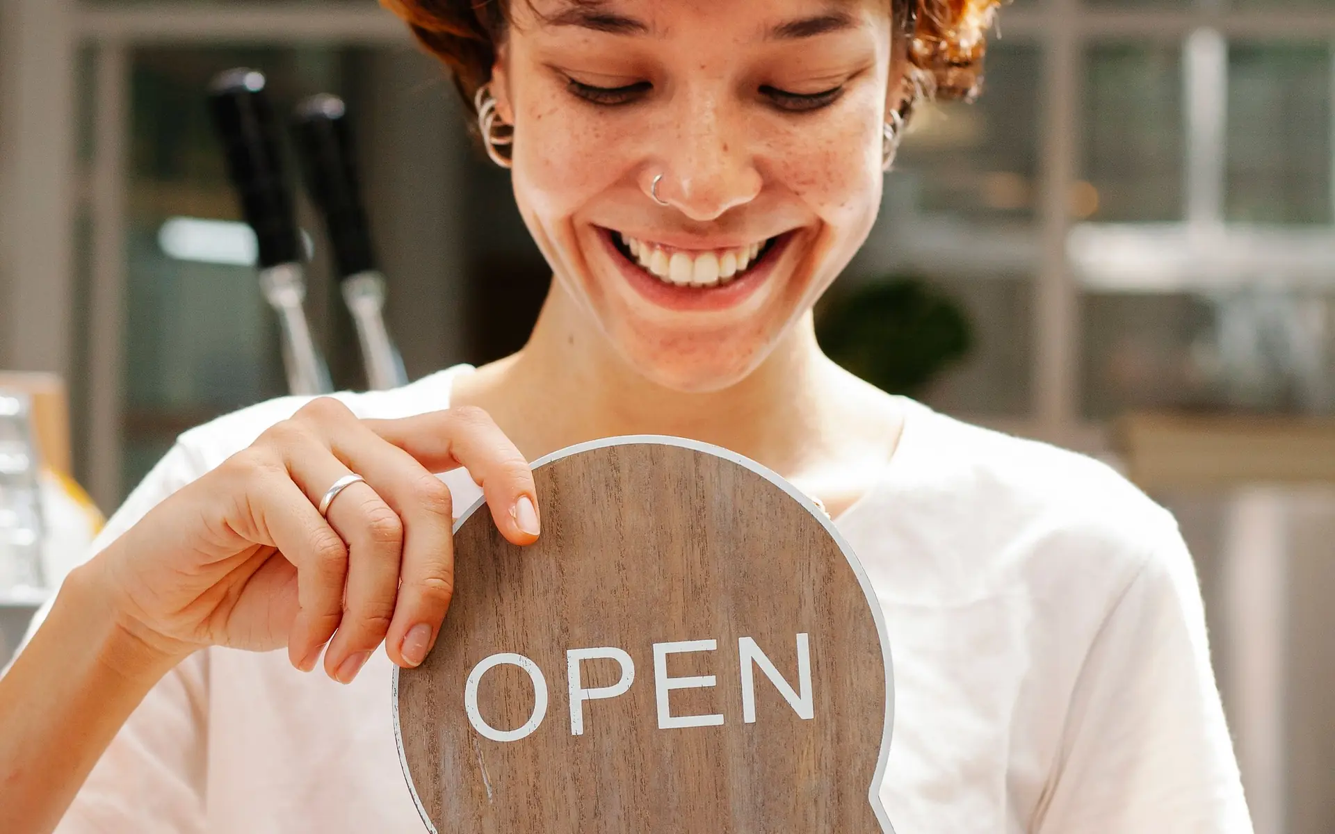 A woman displaying an open sign in a café window.