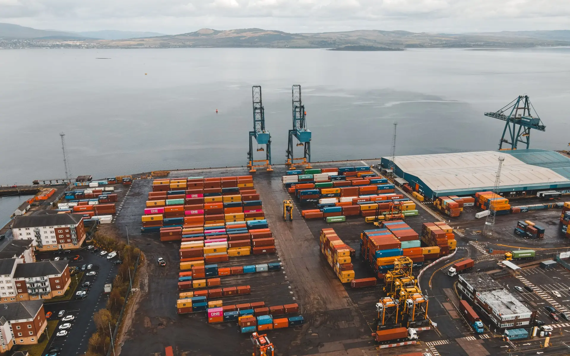 Aerial view of shipping containers and cranes at a coastal port.